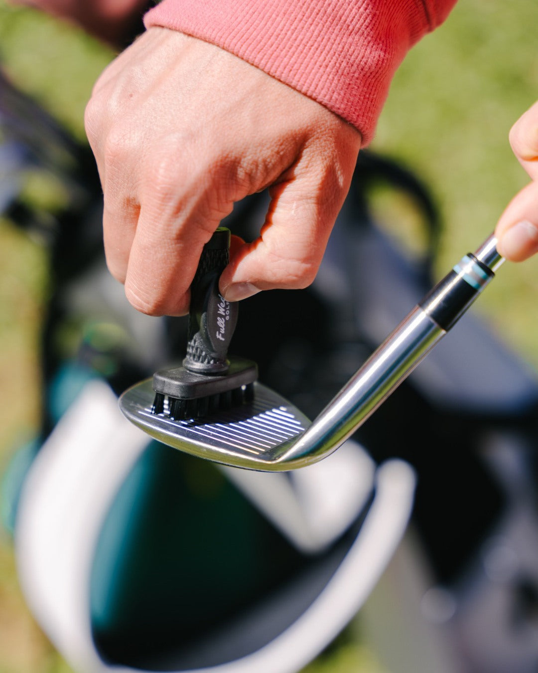 Close-up of a golfer cleaning a club face with a custom mini Grooveit brush featuring the Fully Equipped Golf logo.