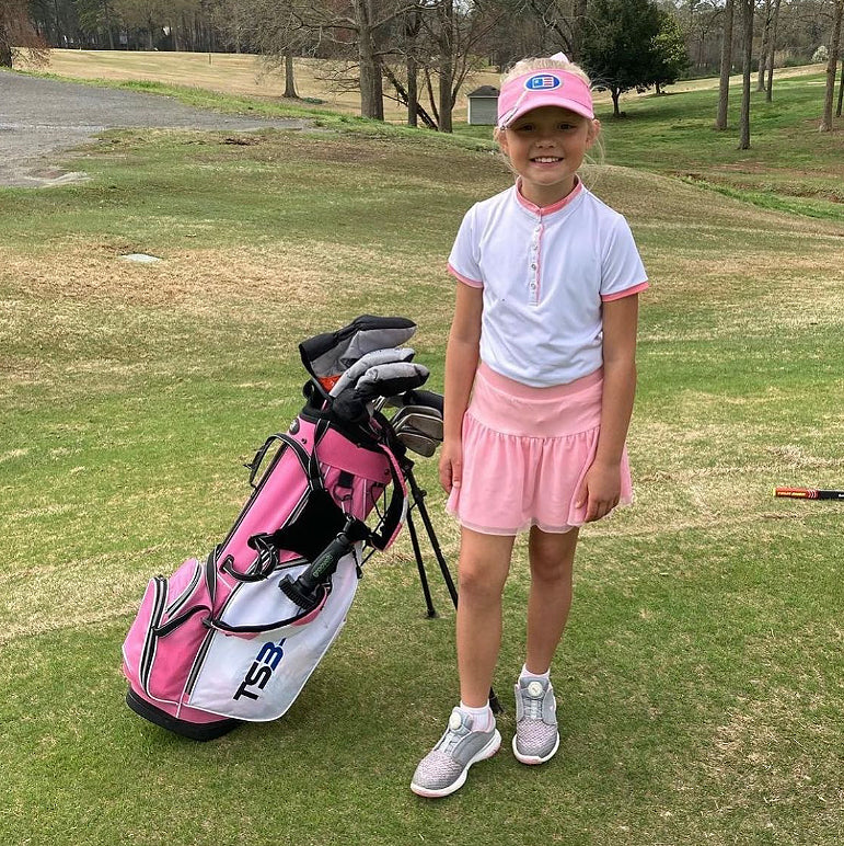 Young girl golfer in pink and white outfit smiling on a golf course next to her pink TS3 golf bag equipped with a Grooveit brush.