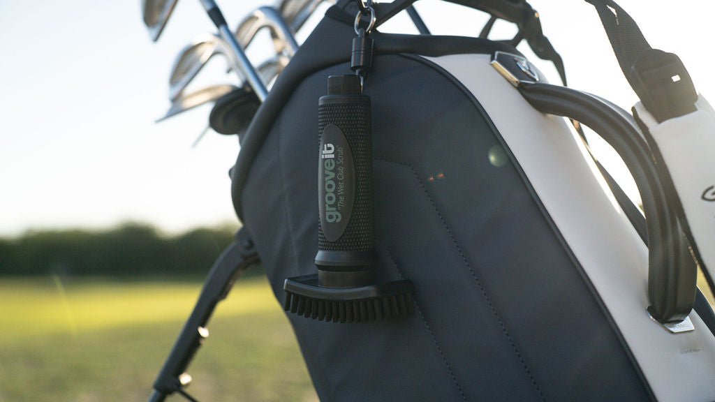 Grooveit golf brush hanging from a golf bag in the sunlight, with clubs visible in the background.