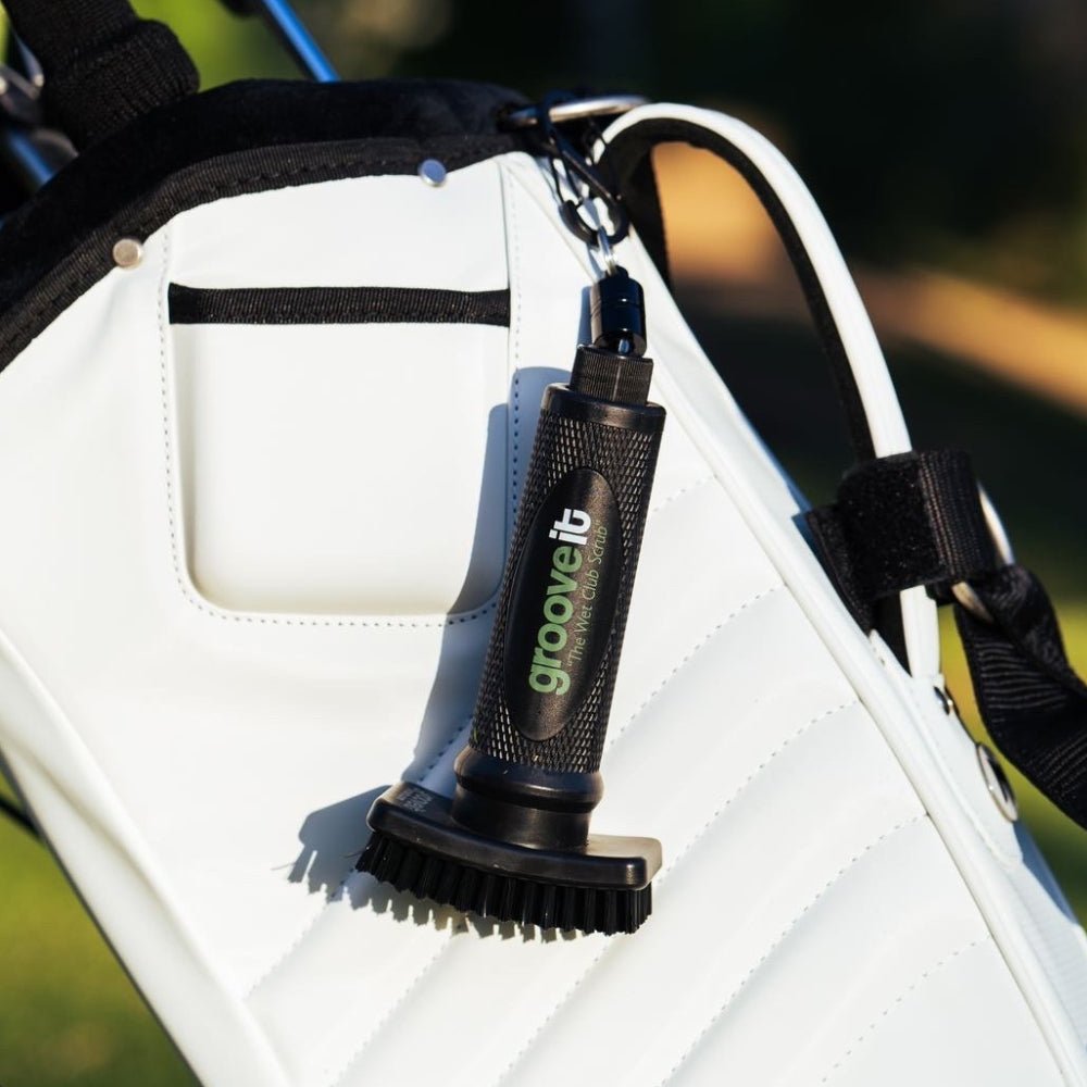 Grooveit “The Wet Club Scrub” golf brush clipped to a sleek white golf bag, shown in sunlight on the course with clear view of bristles and grip.